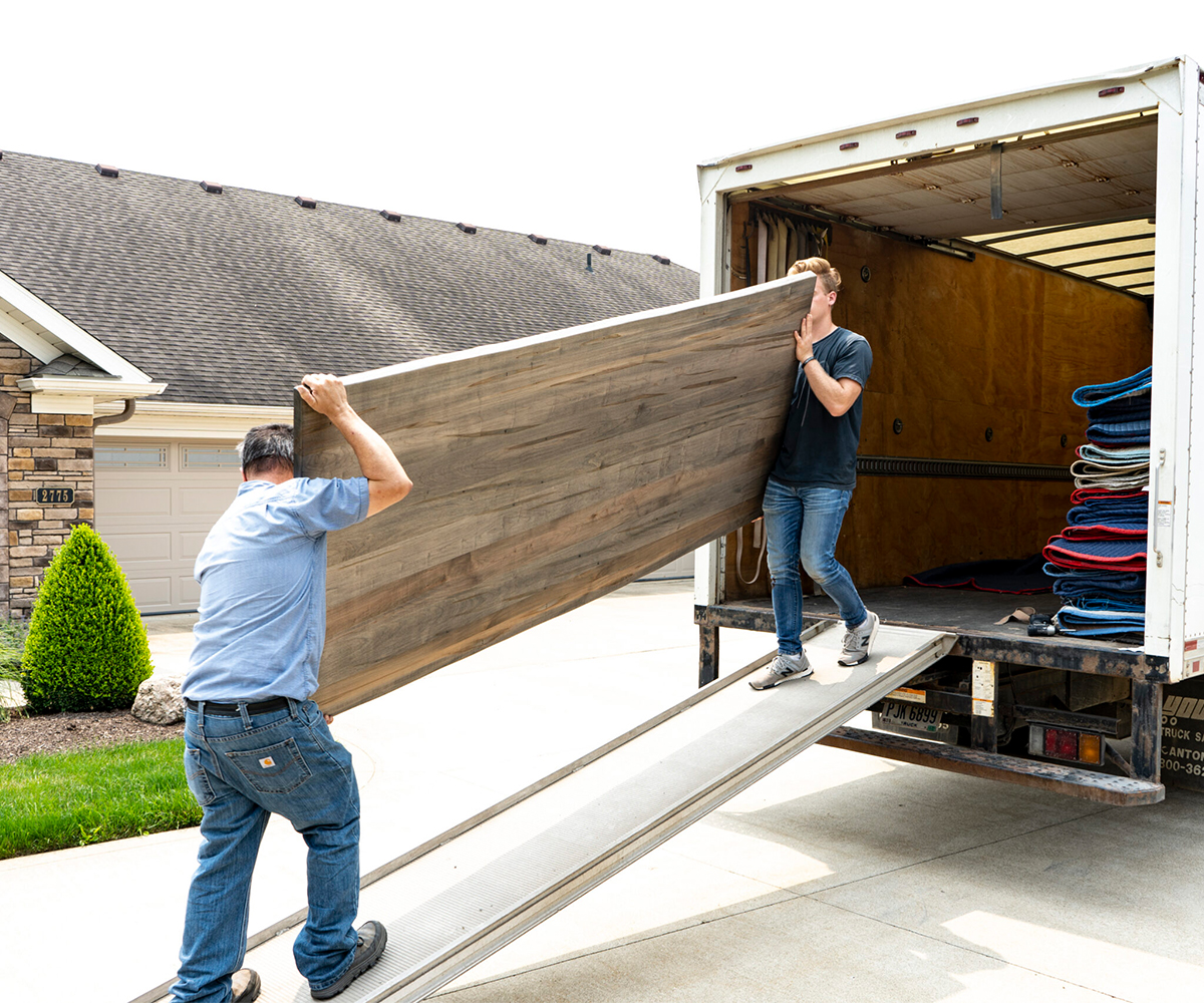 Delivery crew carries solid wood tabletop from truck into a home.