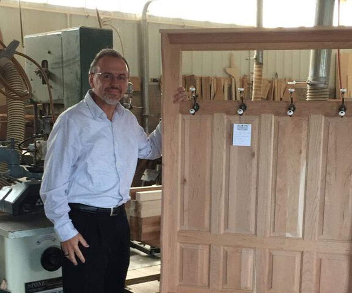 Owner in Amish woodworking shop beside unfinished solid wood cabinet door.